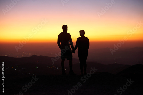 Silhouetted Couple Holding Hands Against a Vibrant Sunset Sky, w