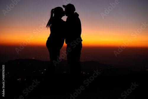 Romantic Silhouette of a Couple Kissing at Sunset, Against a Backdrop of Colorful Sky and Distant Landscape