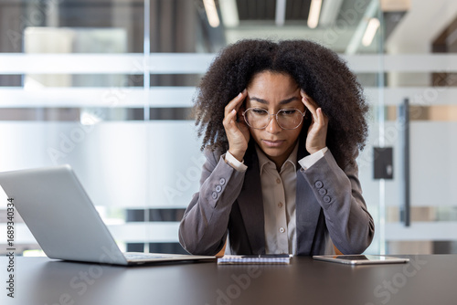Фотография A serious young African American woman sits at her desk in the office, thoughtfu