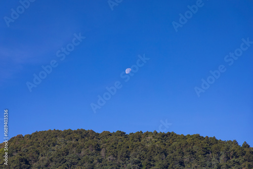 The moon in a blue sky over the mountain.