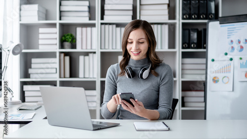 Adult Woman Working From Home Using Smartphone With Laptop and Headphones At Desk - Business Meeting Conference Call or Online Shopping and Banking