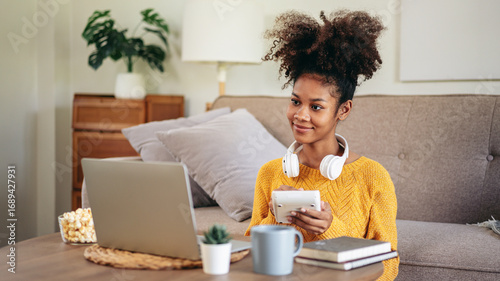 Young Woman Working from Home on Laptop with Calculator and Headphones Smiling Enjoying Popcorn Snack on Coffee Table