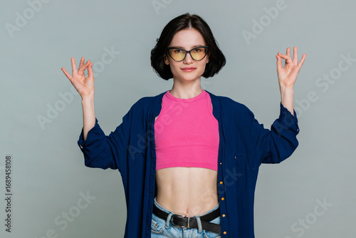 Young woman stands calmly with closed eyes breathing deeply to meditate clearly expressing peaceful relaxation concentration. Caucasian girl demonstrates mindfulness and tranquility on gray background