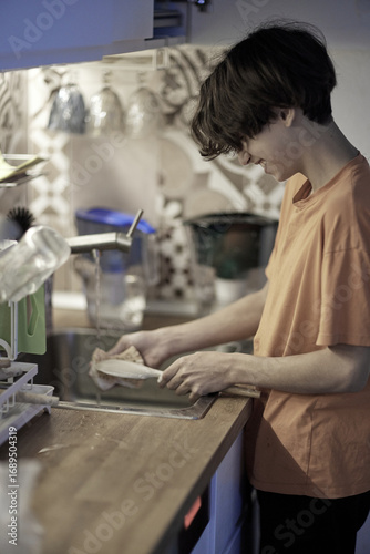 Teen boy washes dishes in cozy kitchen