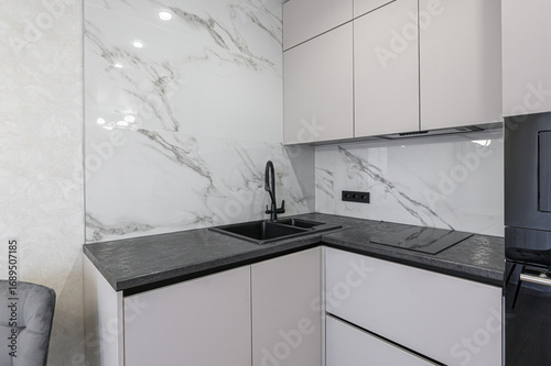 Modern kitchen corner with white cabinets, dark countertops, marble backsplash, and a black sink and faucet. Clean and sleek design