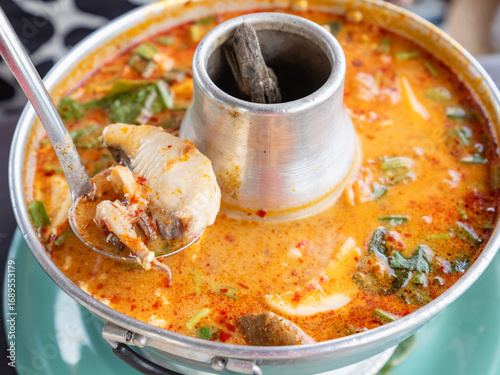Thai seafood soup (Tom Yum Talay) served in a hot pot with fish, shrimp, squid, mushrooms, herbs, and chili in spicy and sour broth.