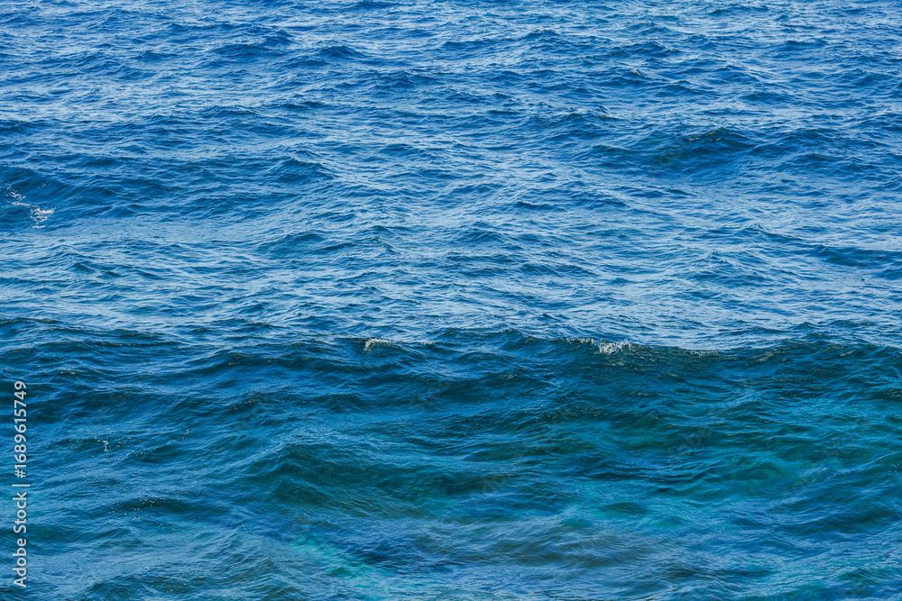 Obraz premium Sea surface aerial view. Background shot of clear sea water surface. Blue sea water in calm. Sea texture. Background blue waves of the ocean