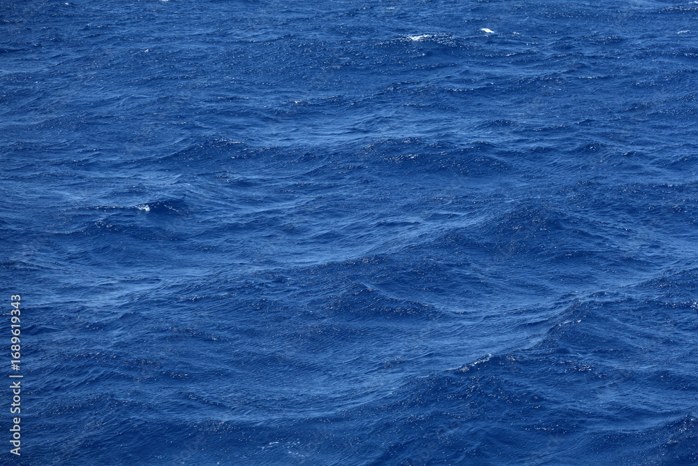Obraz premium Sea surface aerial view. Background shot of clear sea water surface. Blue sea water in calm. Sea texture. Background blue waves of the ocean