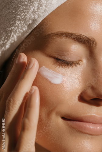 A woman demonstrating facial cream on her skin, using fingers for precise application.