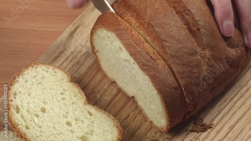 Close-up of young woman slicing fresh white bread with a kitchen knife on a cutting board in her kitchen, recorded with ambient sound.