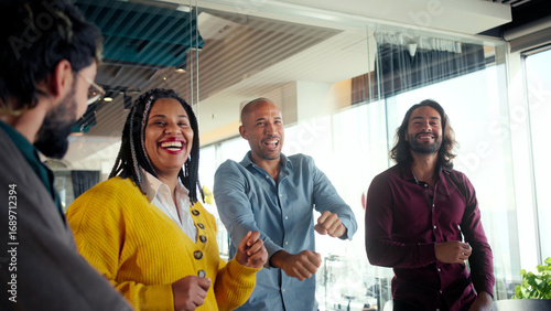 Fotografie Smiling colleagues celebrate together during a playful team building moment in a bright modern office, showing inclusion, motivation, unity and positive energy that strengthens workplace culture