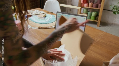 Close up shot of tattooed young woman packing small decorative rug into box while managing online shop side hustle and shipping orders, copy space