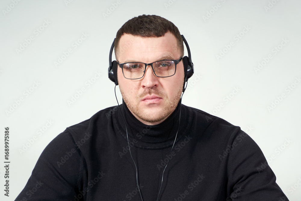 Obraz premium concentrated man in headphones using laptop while sitting over grey background