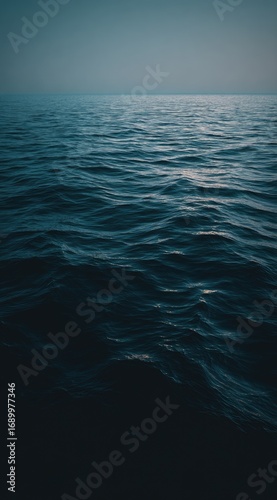 Deep blue ocean view under a misty sky, with gentle waves creating a soothing, rippled texture. The dark water fades into a soft, hazy horizon