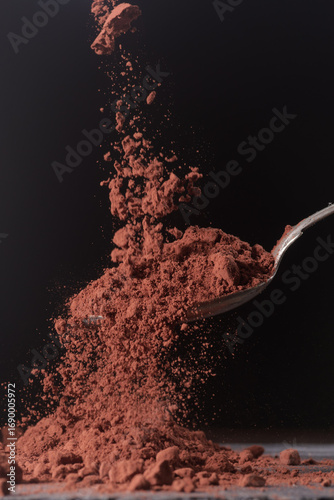 Dark cocoa falling onto a spoon. Scene shown against a dark background