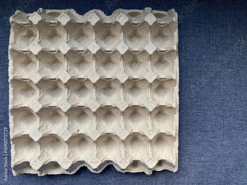 empty grey paper egg tray on a clean dark blue fabric background with copy space on the right of the frame