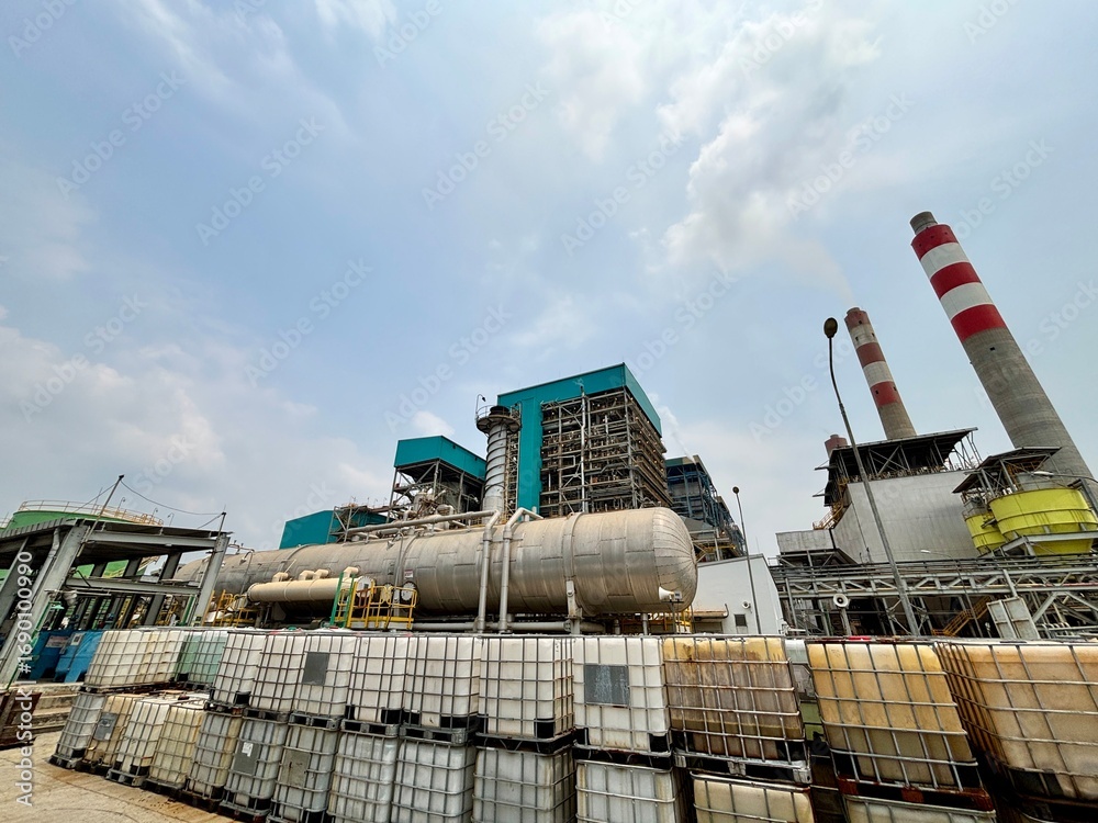 Obraz premium Industrial landscape showing a power plant with storage containers under a cloudy sky highlighting the intersection of energy production and logistical infrastructure in a commercial setting