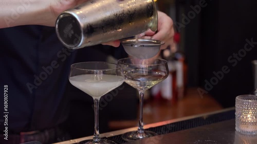A skilled bartender artfully pours a delightful cocktail into elegant, shimmering glasses using a stylish shaker