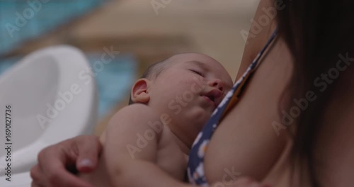Infant baby girl in mothers arms next to tropical pool - close up