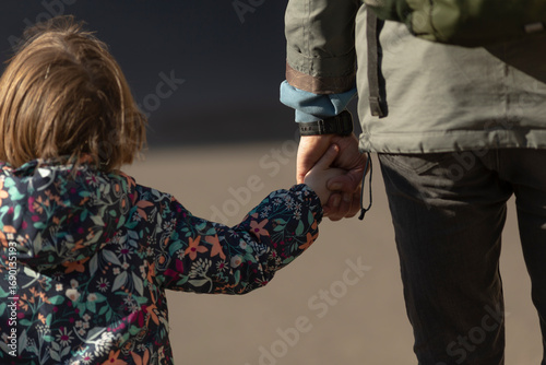 A child and an adult are walking hand in hand in an urban setting, enjoying their time together