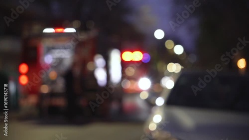 Defocused image of a fire truck flashing emergency lights in an urban setting at night.