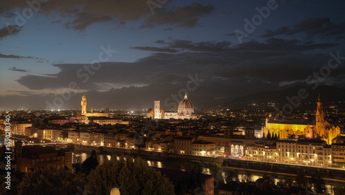 Florence, Italy at night with illuminated cathedral, Arno River reflections, and historic city skyline.