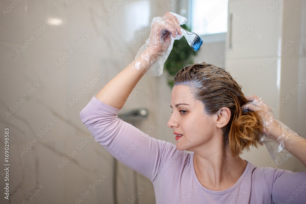 Fototapeta premium Woman dyeing her hair at home in the bathroom