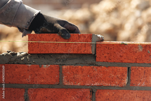 Skilled worker laying red bricks in a construction site during daylight with focused attention on building a wall