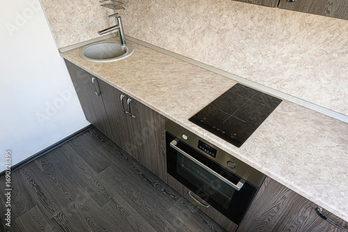 modern kitchen corner featuring a sink, cooktop, and oven built into dark wood cabinets with a light countertop and dark flooring