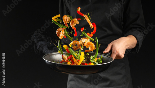 Chef tossing shrimp and vegetables in a frying pan against black backdrop