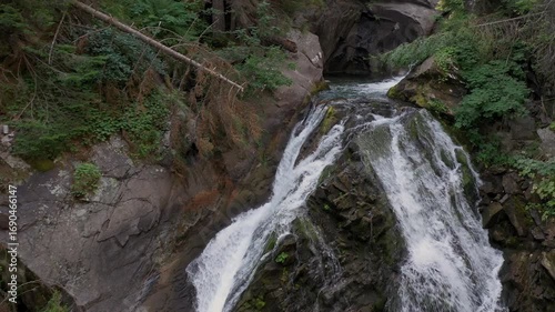 Aerial view, drone descent back flight over medium size beautiful waterfall in Pirin Mountain in Bulgaria, Europe around evergreen coniferous forest.