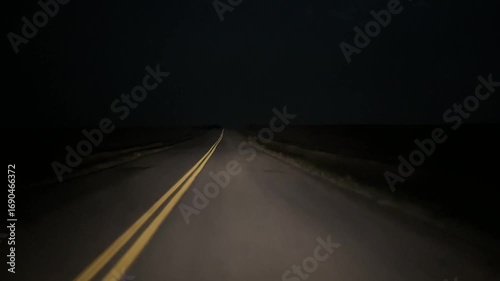 Driver’s point of view while driving at night along a quiet rural highway under dark sky with headlights illuminating the road