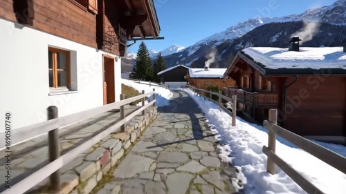 Scenic pathway through a snowy village with wooden chalets and majestic mountains in the background