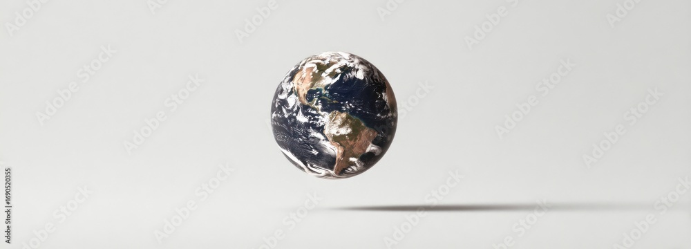 Obraz premium A floating globe of Earth with visible continents and swirling clouds, casting a shadow on a plain white surface