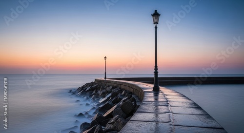 Tranquil ocean sunrise with lamp posts on curved stone pier