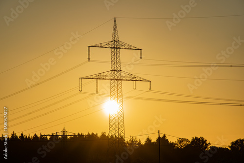 Transmission tower or high-voltage electricity pylon with sun shining through steel frame at sunset. Symbol of energy and power generation.