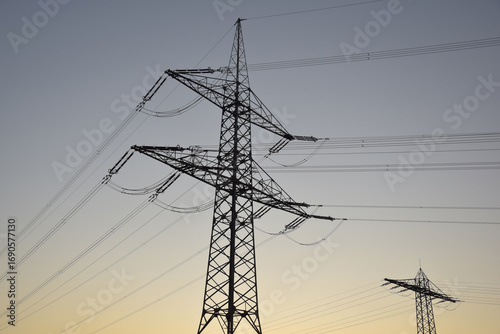 High-voltage electricity pylon photographed from below at blue hour shortly after sunset, silhouetted against the evening sky in Germany.