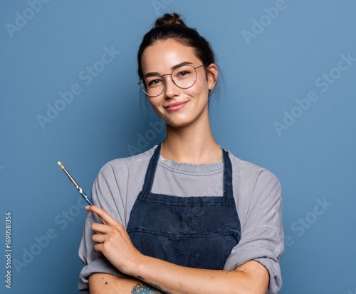 Confident female  holds a paintbrush, showcasing a creative and artistic persona against a simple backdrop.