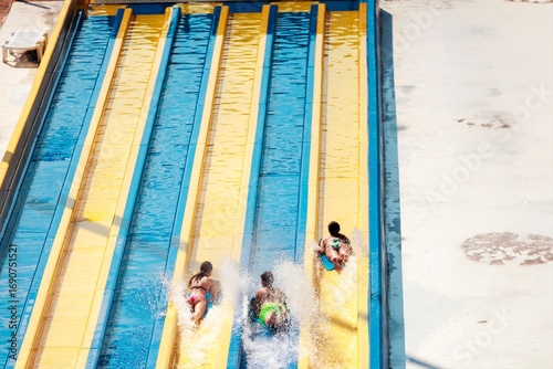 Картината върху платно Three people are riding individual brightly colored blue and yellow water slides