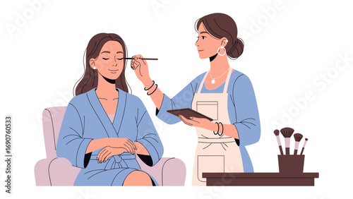 Professional makeup artist applying foundation to a woman sitting in a chair wearing a blue robe in a beauty salon