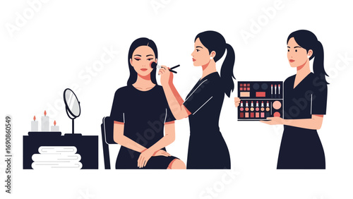 Professional makeup artist applying cosmetics to a client while an assistant holds a makeup palette and beauty products in a salon setting