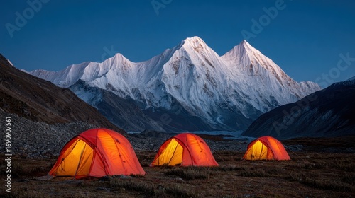 Illuminated orange tents nestled at the base of snow-capped mountains at dawn