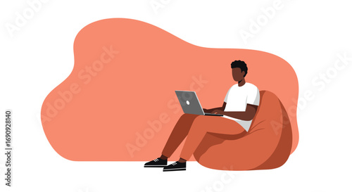 Young man working on laptop from home, sitting comfortably on a bean bag chair. Ideal for remote work, freelance, or online education concepts.