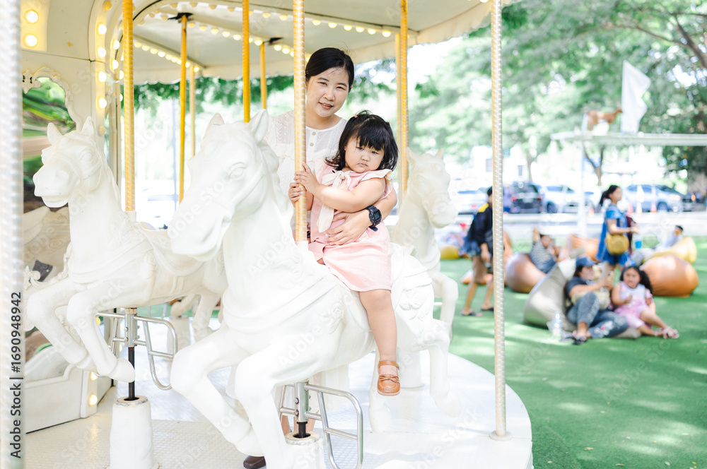Obraz premium Asian mother and daughter riding a carousel in an amusement park.