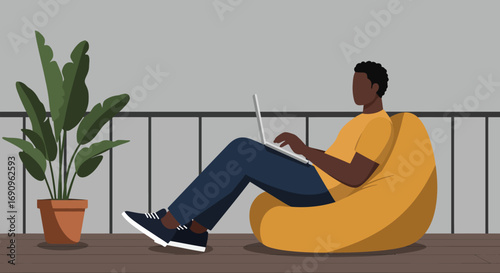 African American man working remotely on a laptop, comfortably seated on a yellow bean bag on a modern balcony, embodying flexible work and modern lifestyle.