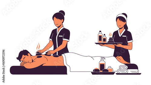Professional spa therapist performing hot stone massage on a relaxed client with another therapist holding a tray of massage oils and towels
