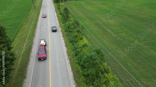 Aerial Drone footage of car driving along a rural road with green fields and trees