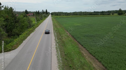 Aerial Drone footage of car driving along a rural road with green fields and trees