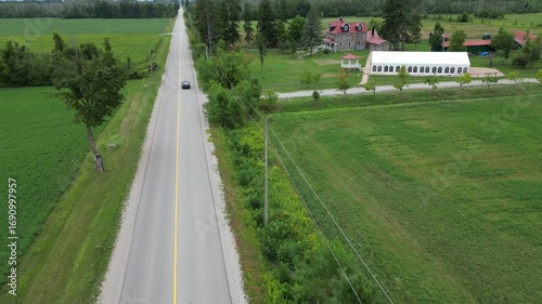 Aerial Drone footage of car driving along a rural road with green fields and trees