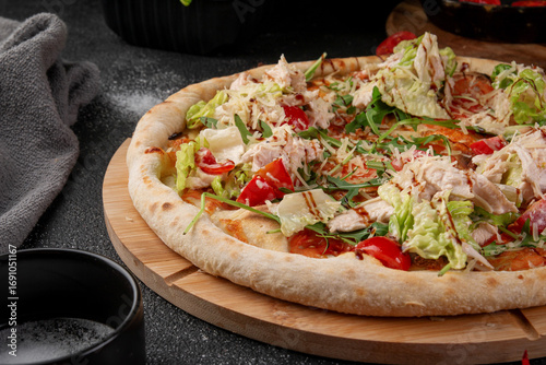 Fresh Caesar pizza topped with sliced chicken breast, lettuce, cherry tomatoes, arugula and grated parmesan on wooden board